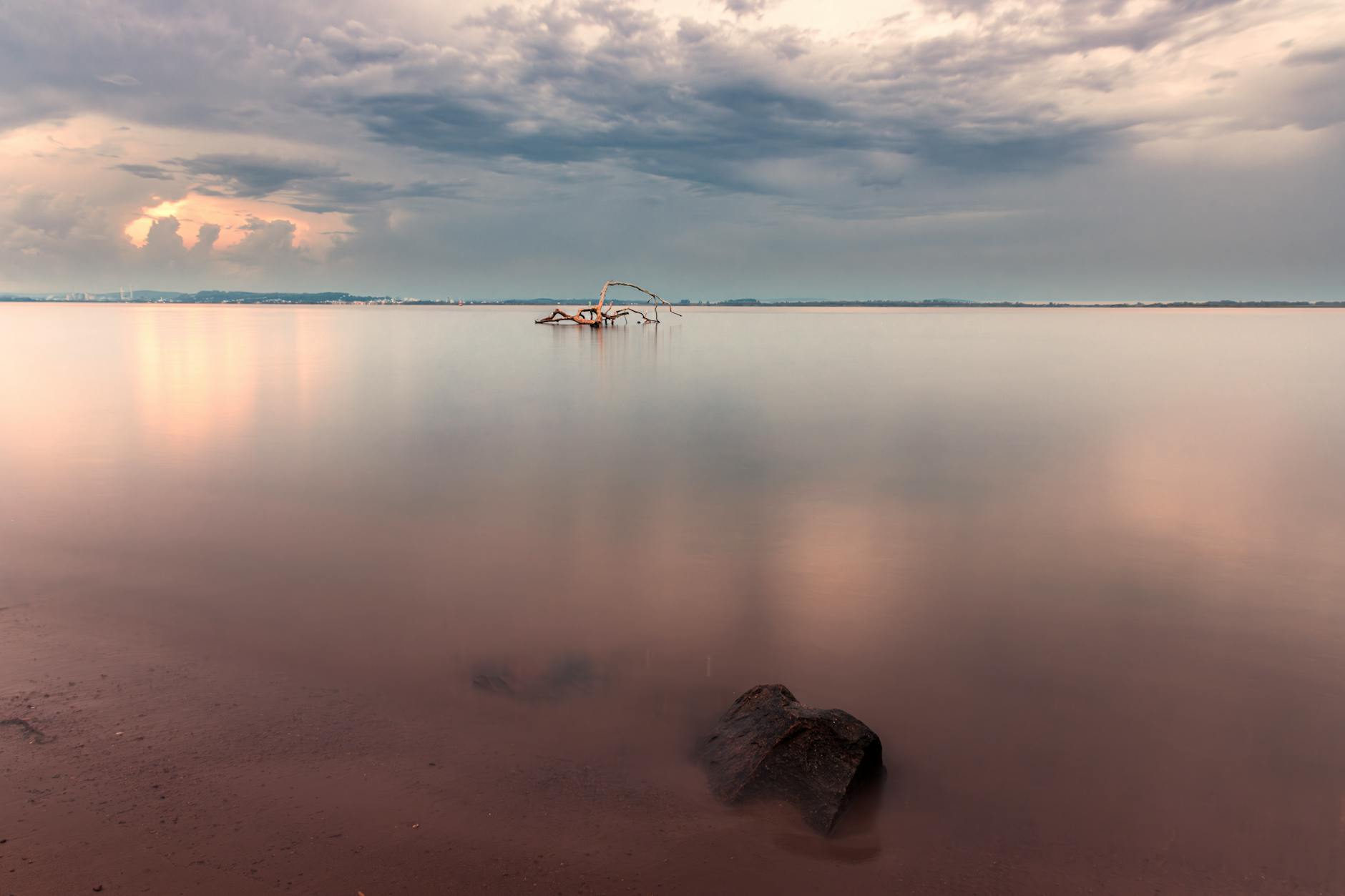 Peaceful scene of Porto Alegre's coastline at sunset with calm waters and distant cityscape.