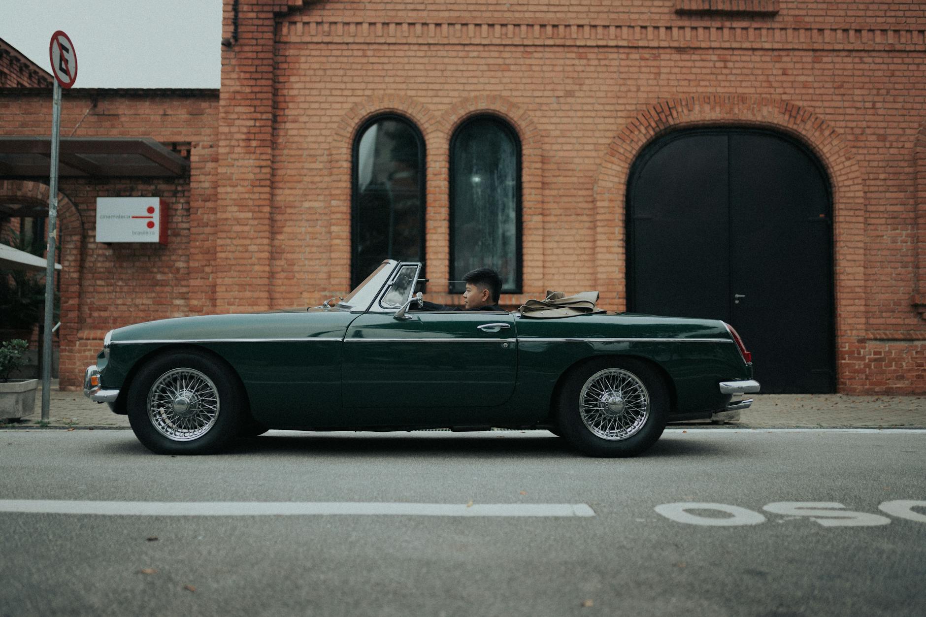 Classic green MG MGB convertible on São Paulo streets with brick backdrop.