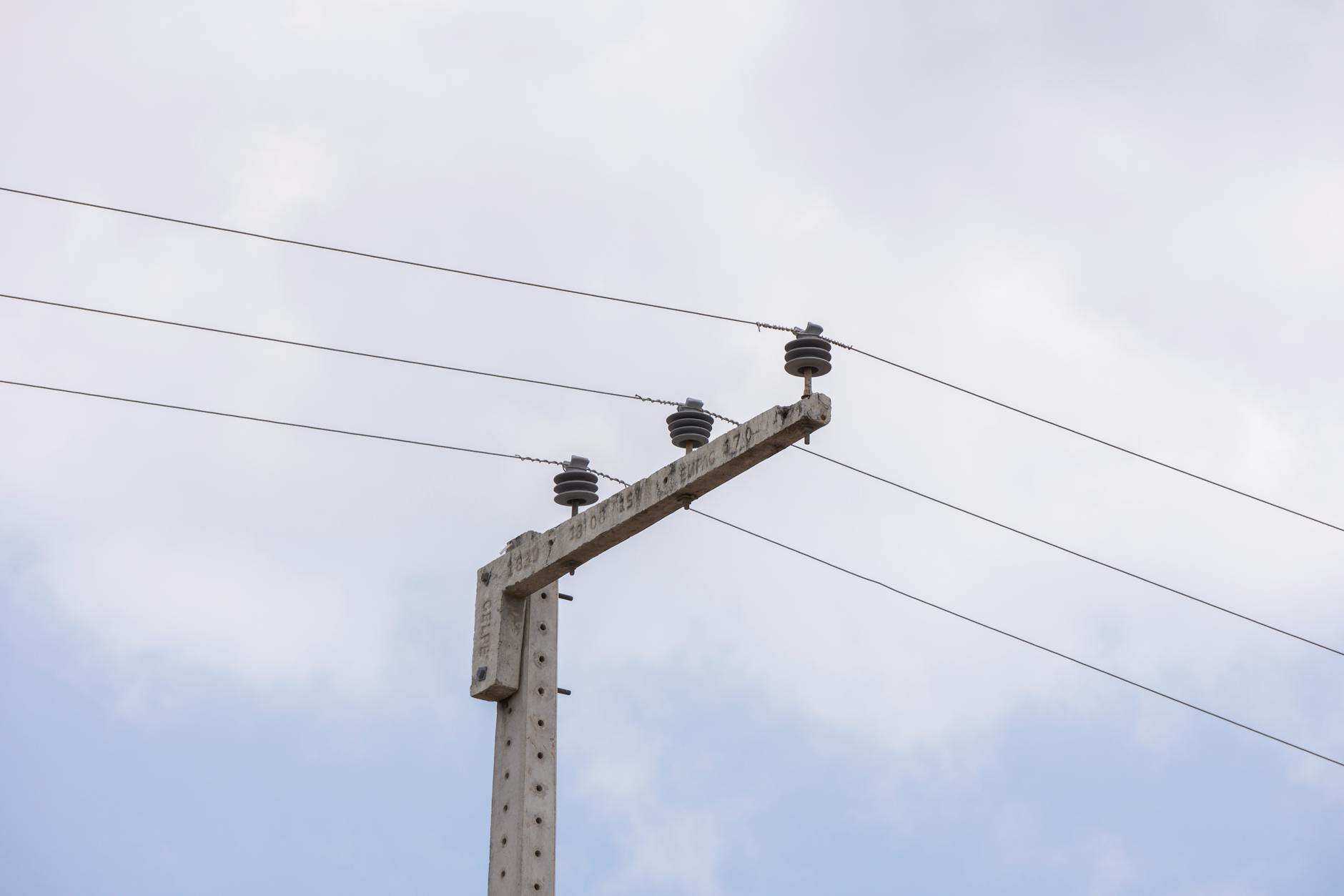 Concrete utility pole with wires against a cloudy sky, highlighting urban infrastructure.