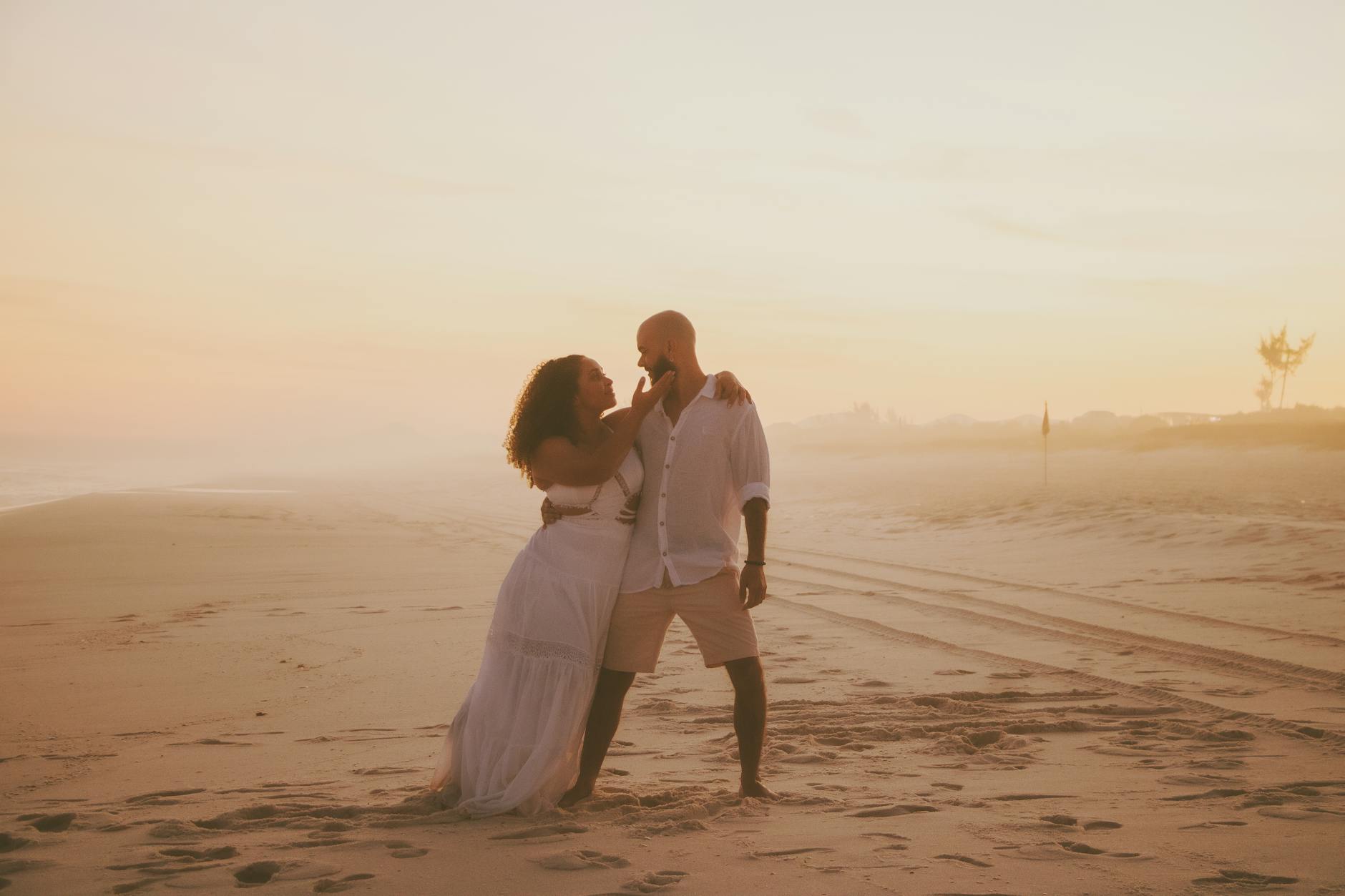 A couple shares a romantic moment on a sandy beach in Rio de Janeiro at sunset.