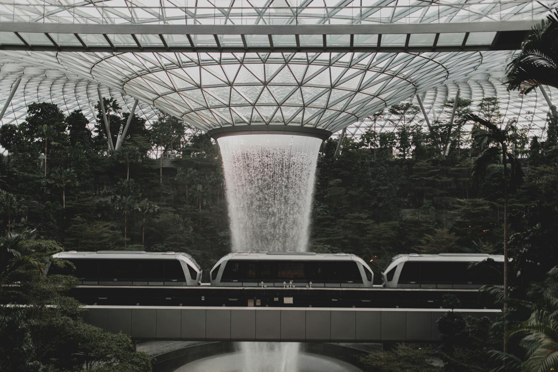Contemporary rail link train going under indoors waterfall streaming from creative glass ceiling in Jewel Changi Airport in Singapore