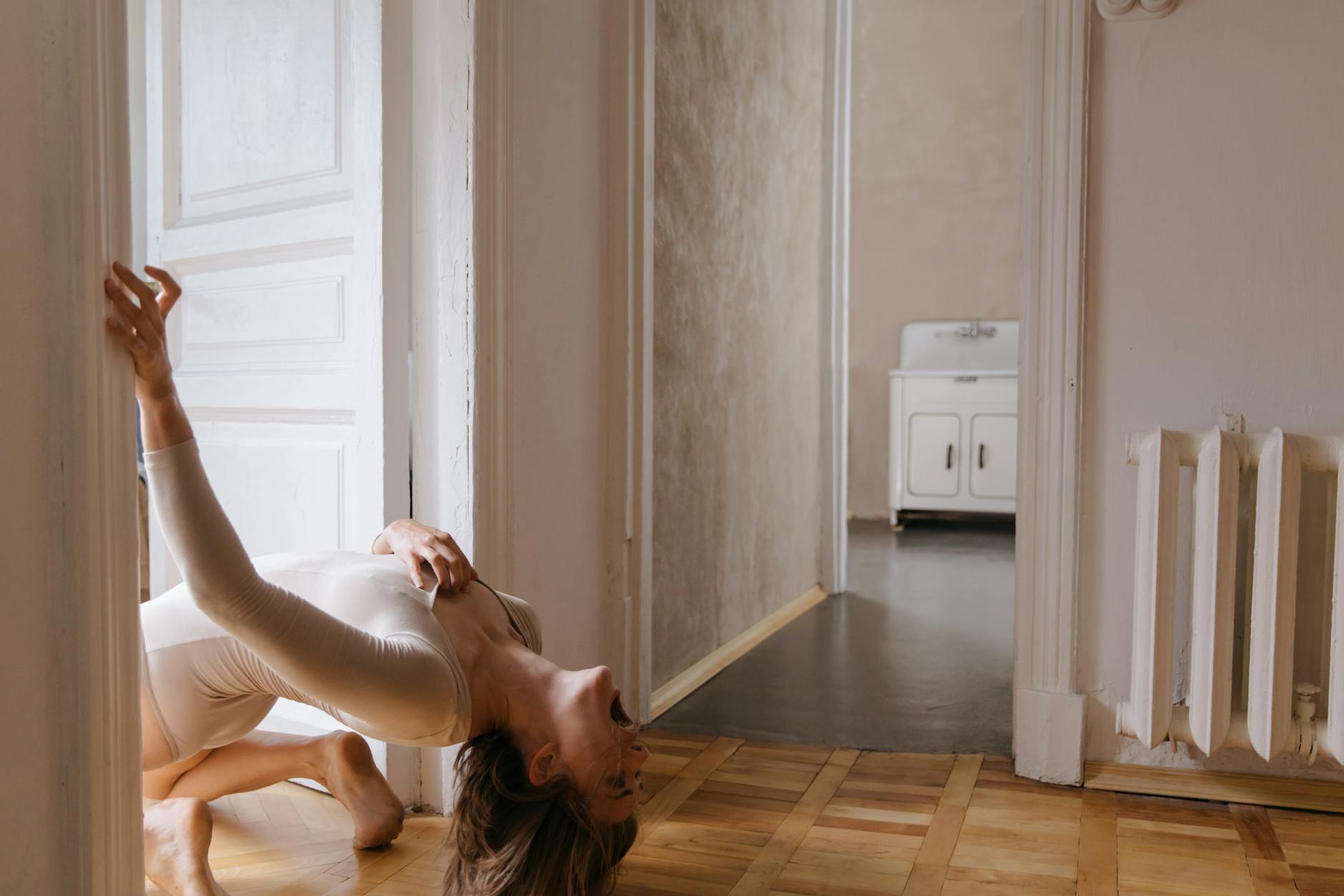 A woman in a dynamic pose inside a minimalist room creating an artistic expression.