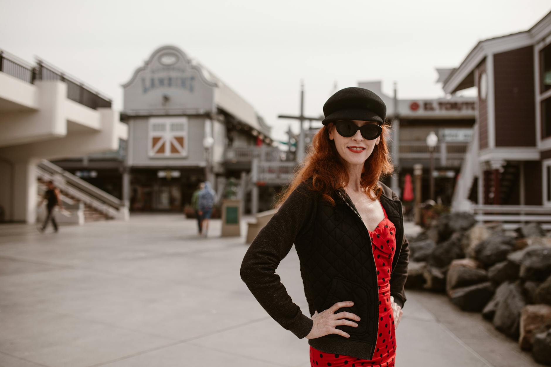 A fashionable woman in sunglasses and a black hat poses confidently in a city street.