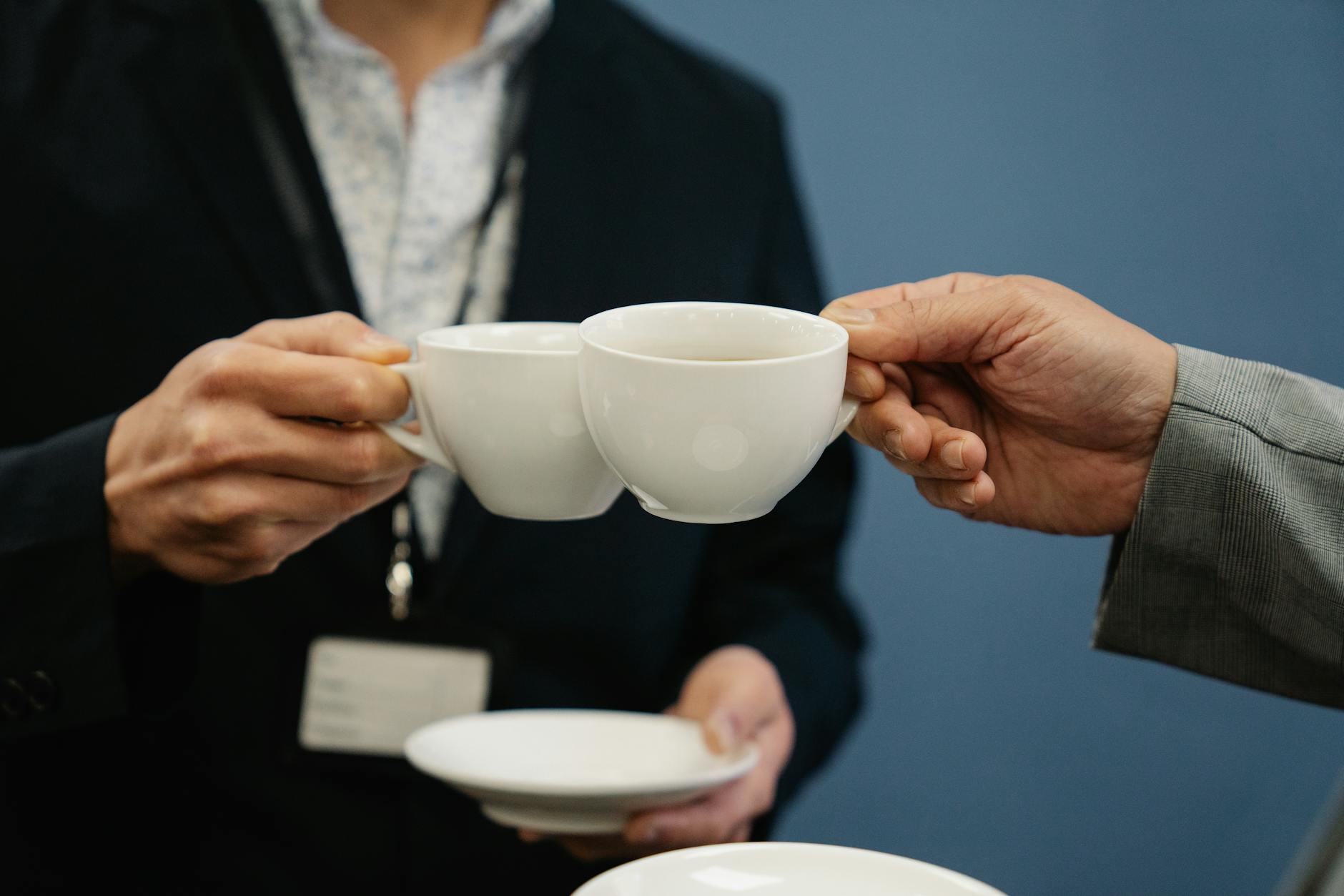 Close-up of two business professionals clinking coffee cups in an office setting.
