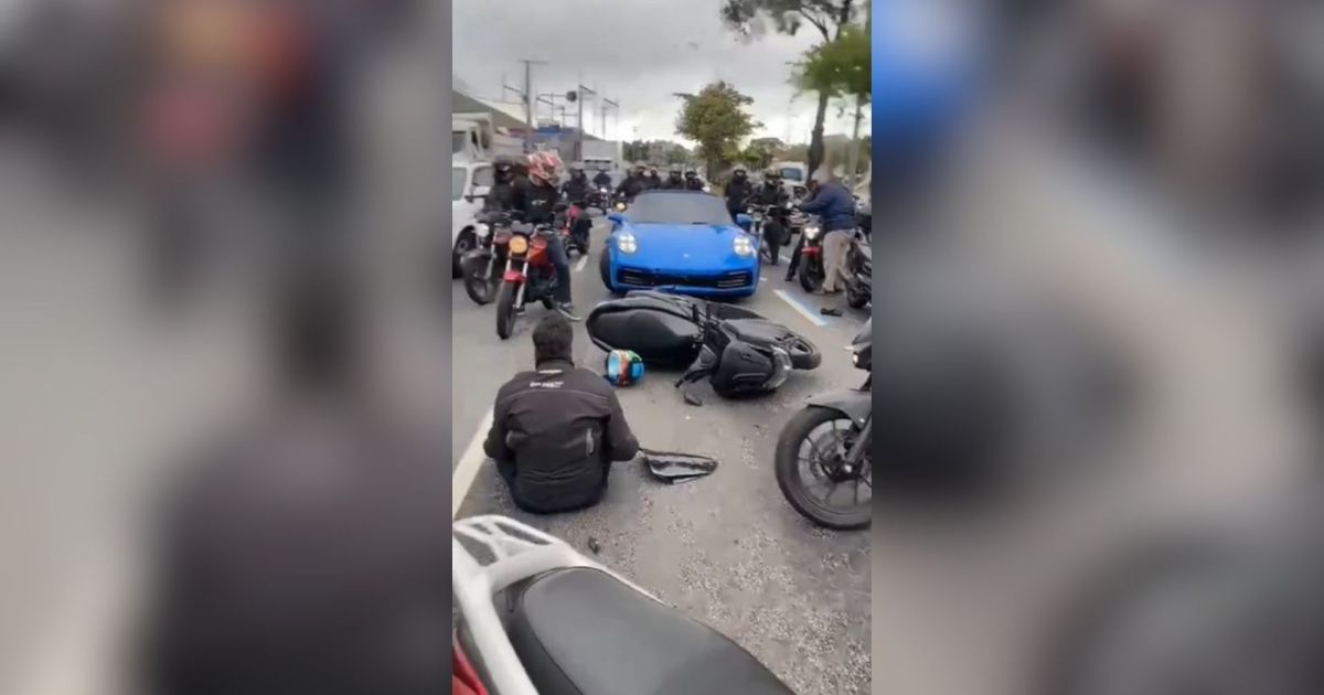 Carro esportivo de luxo parado em avenida movimentada, com motocicletas e pessoas ao redor após um incidente de trânsito.