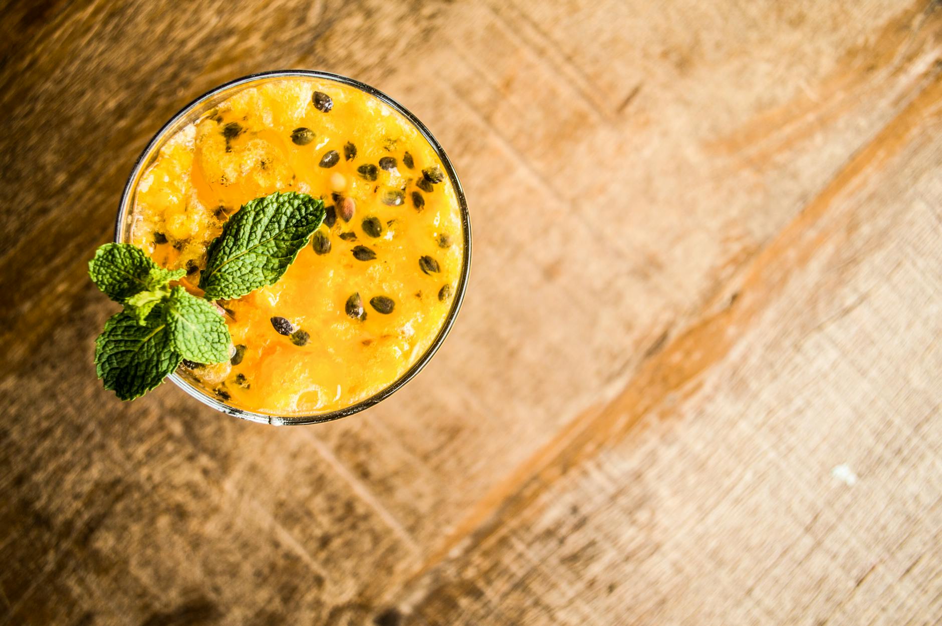 Top view of a refreshing passion fruit drink garnished with mint leaves on a rustic wooden table.