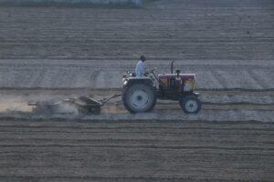 A farmer operates a tractor for harrowing soil in a vast field, capturing early morning labor.