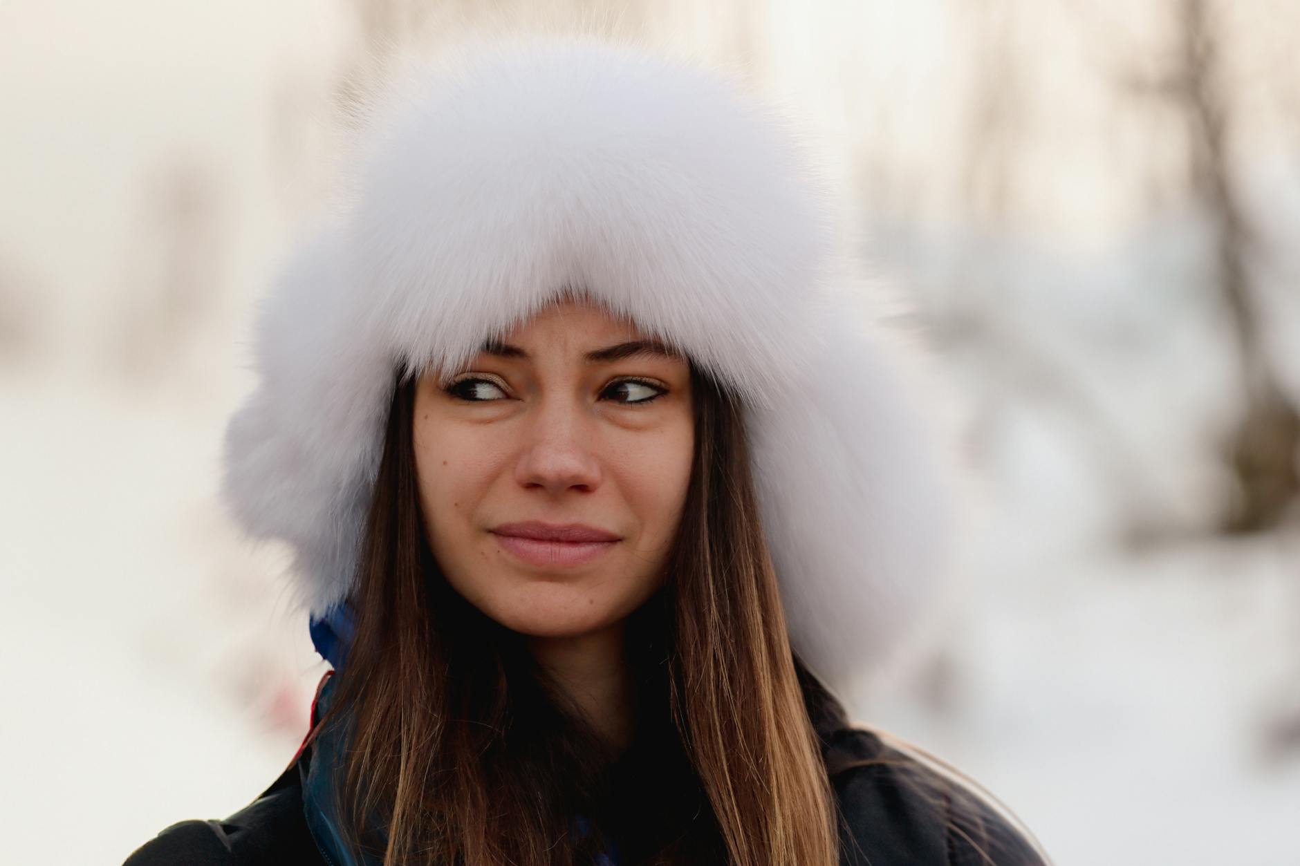 A woman in a white fur hat stands in a snowy arctic landscape in Tromsø, Norway, during winter.