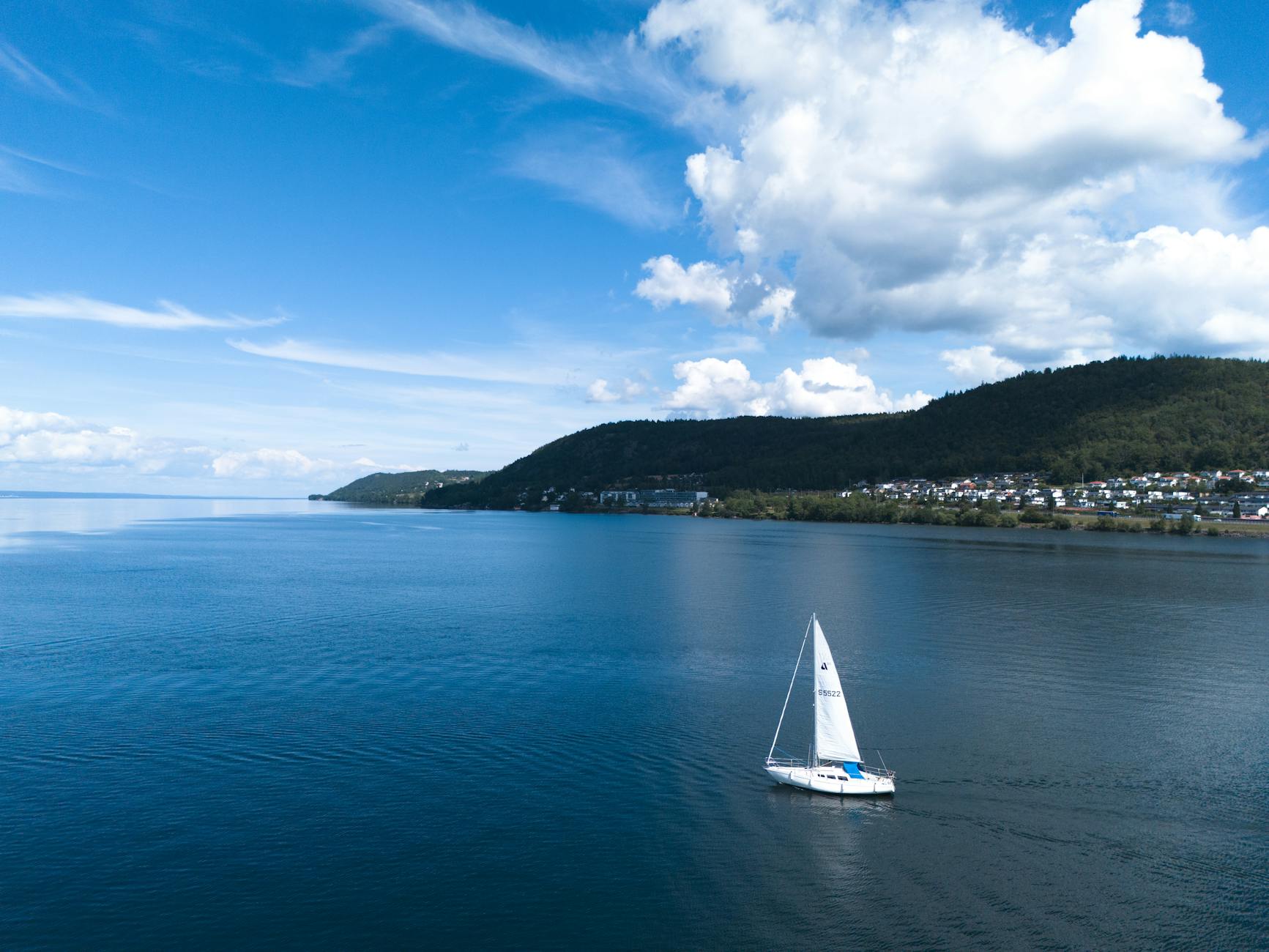 Aerial drone shot of a sailboat on calm blue waters near a lush green coastline in France.