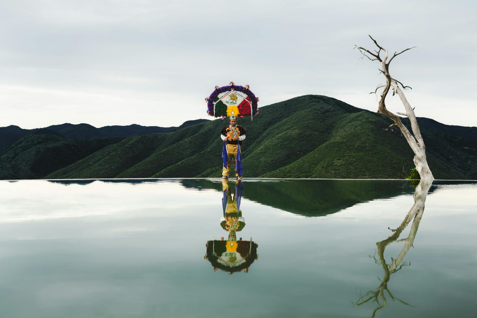 A traditional dancer at Hierve el Agua in Oaxaca, standing against hilly landscapes and reflective waters.