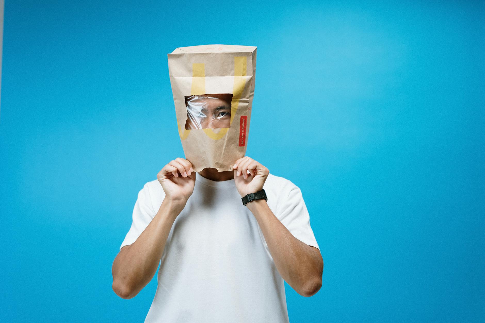 A man humorously wears a DIY protective bag mask against a blue background.