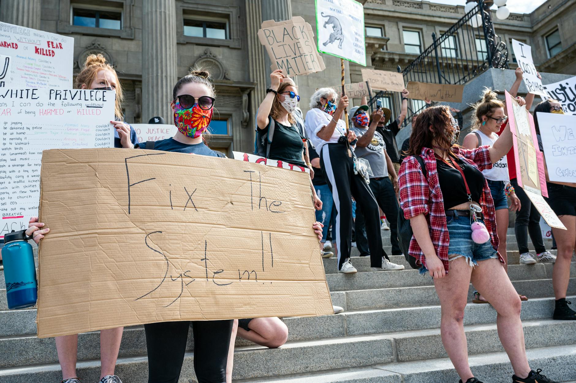 A diverse group of masked protesters demand social justice with signs on city steps.