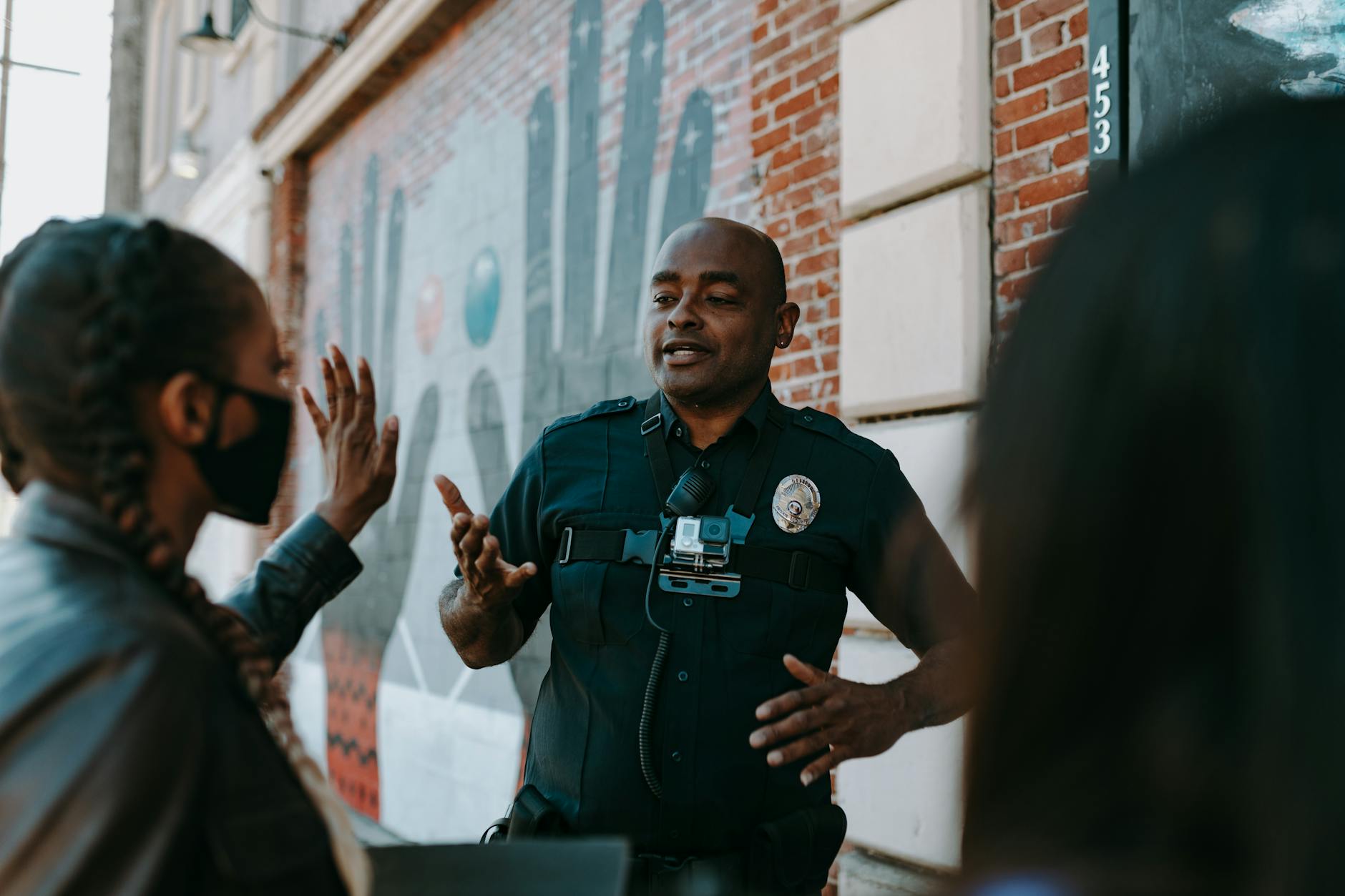 Police officer conversing with people on the street near a brick wall mural.