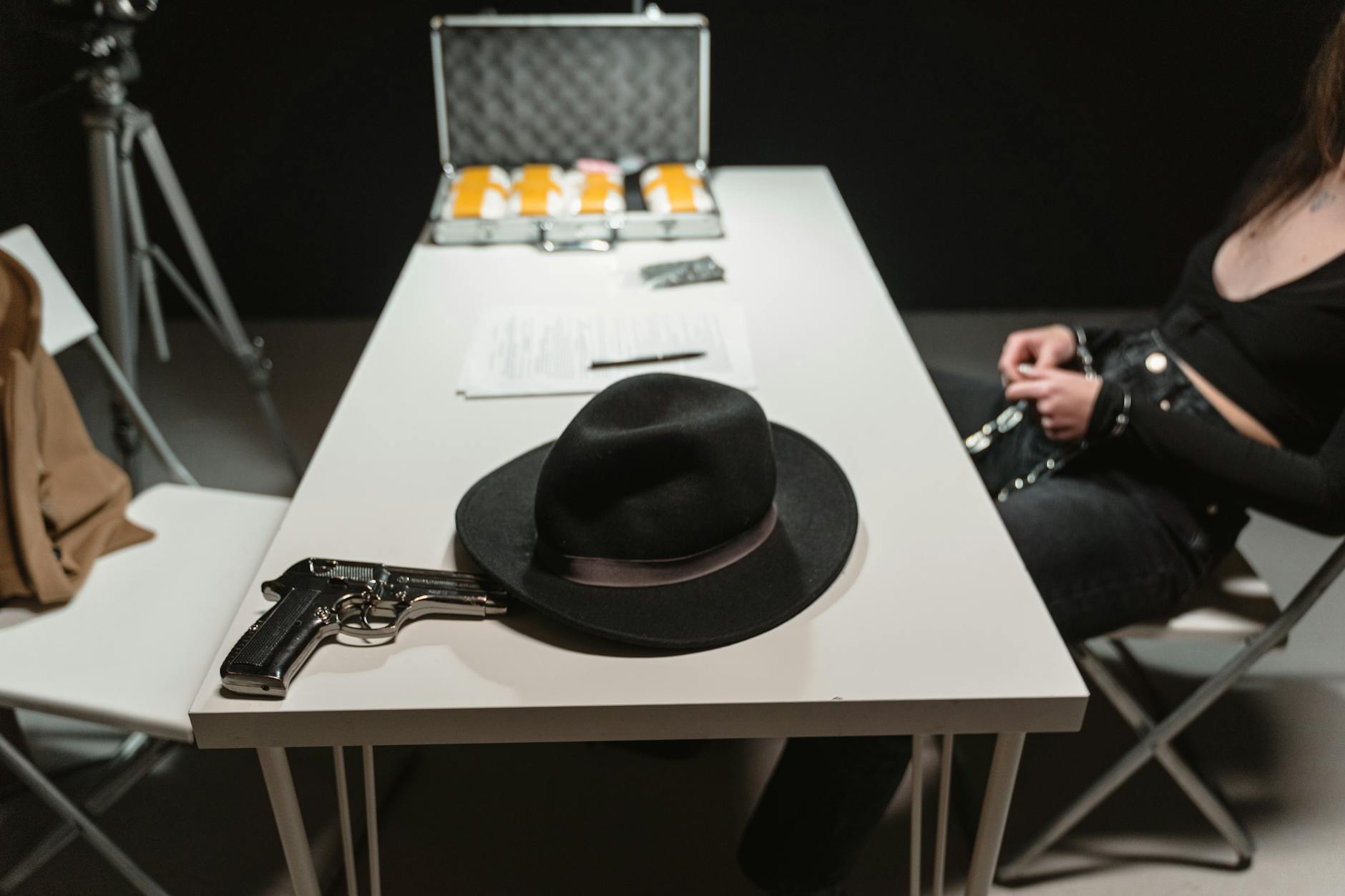 Close-up of a gun and hat on a table in an interrogation room, suggesting a crime scene.