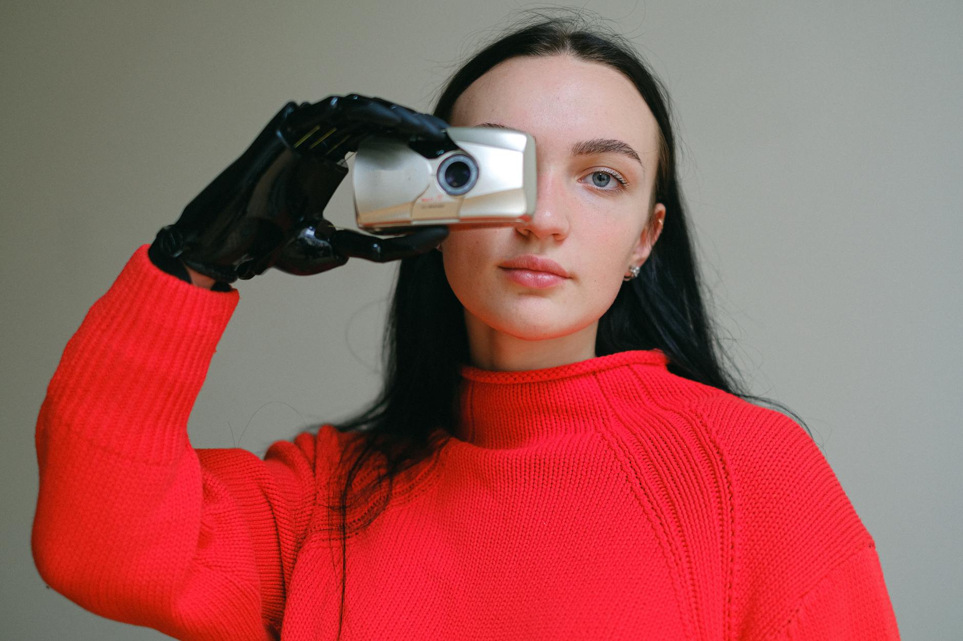 Young woman with a prosthetic hand holds a camera, wearing a red sweater.