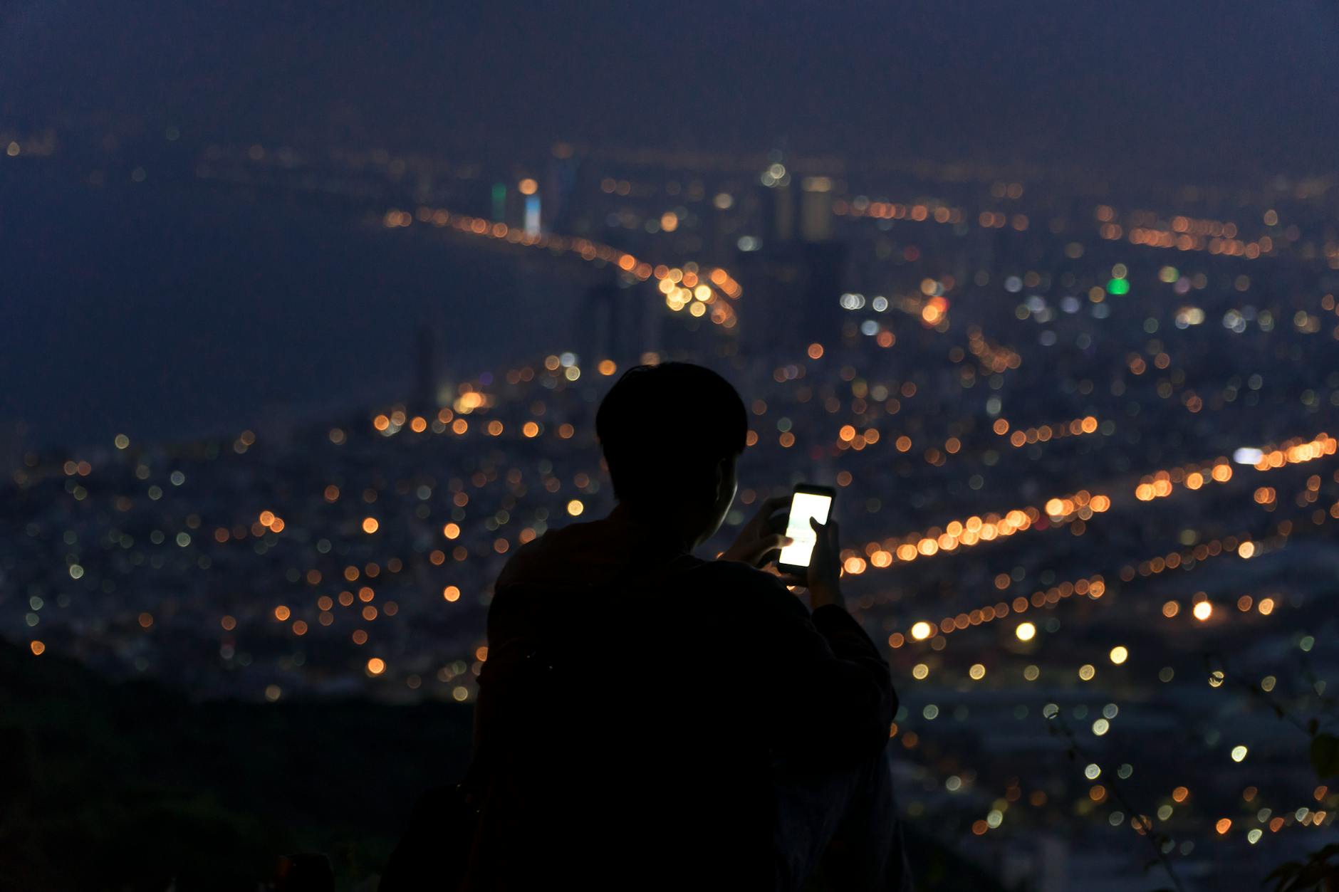 Silhouette of a person using a smartphone against the night skyline of Da Nang, Vietnam.